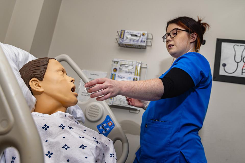 A nursing student gives medicine to a mannequin in the nursing lab. 