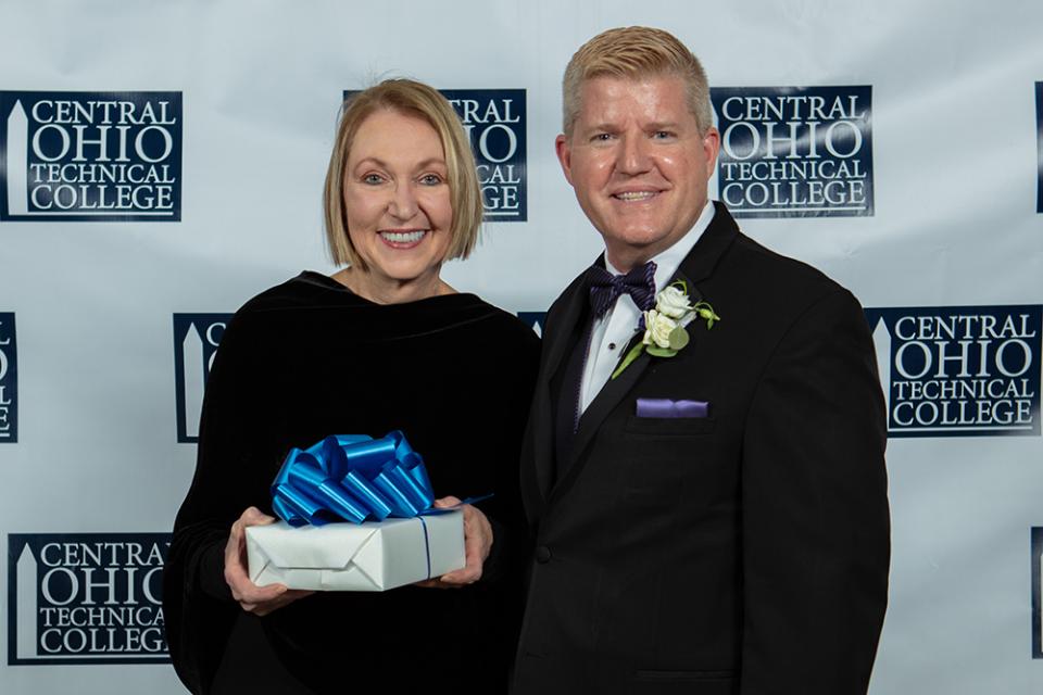 Cheryl Snyders holds the Legends of Loyalty award gift box standing next to COTC President John Berry. 