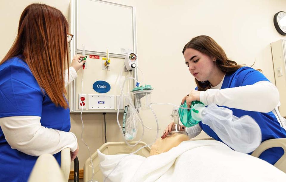 COTC students in a respiratory therapy lab. A student places a breathing apparatus on a mannequin while another student adjusts a dial on a mounted machine during lab at COTC.