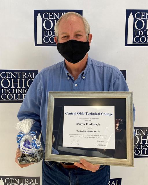 older white male wearing mask holding award in front of camera
