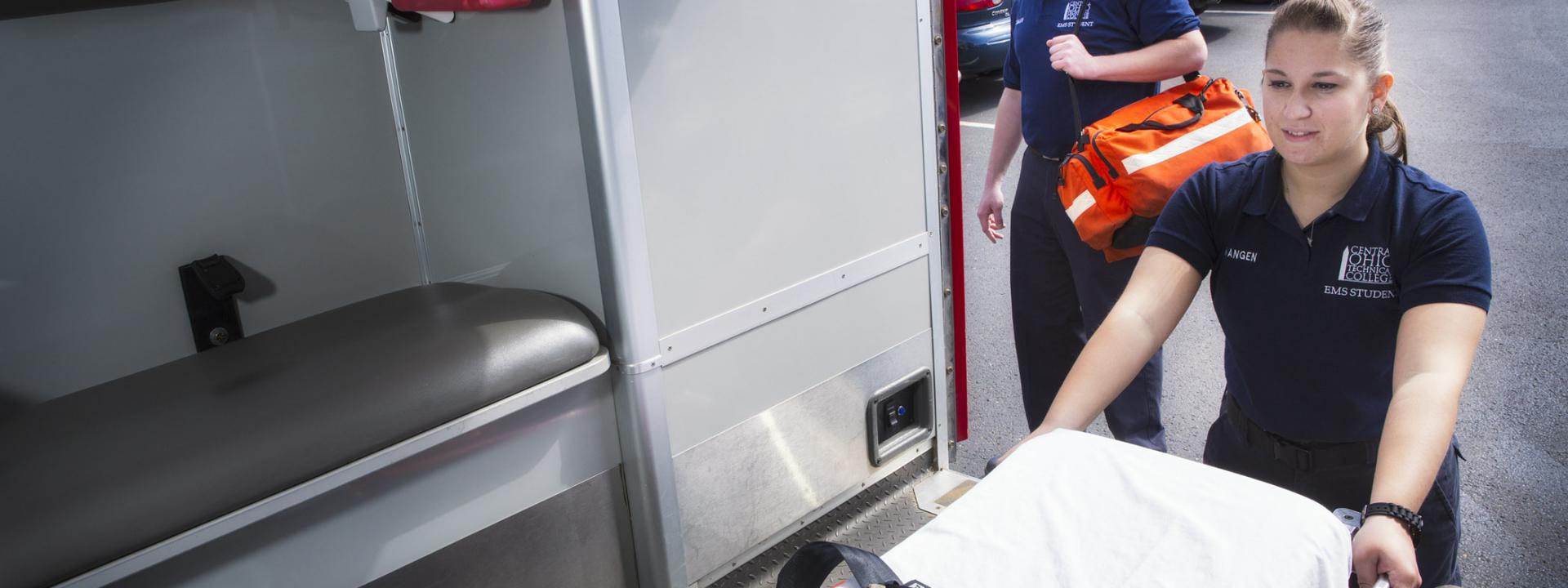 Student taking gurney out of the back of ambulance