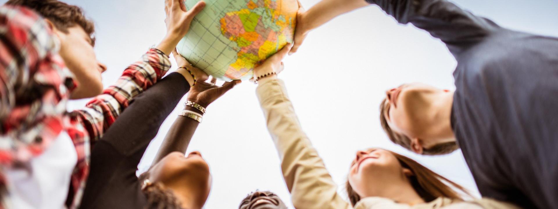 Five people place a hand on a globe positioned above their heads. 