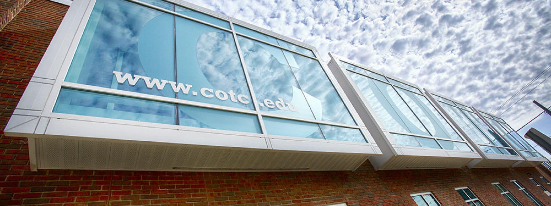The brick exterior of Ariel Hall with a large upper floor window that has a C for COTC. 
