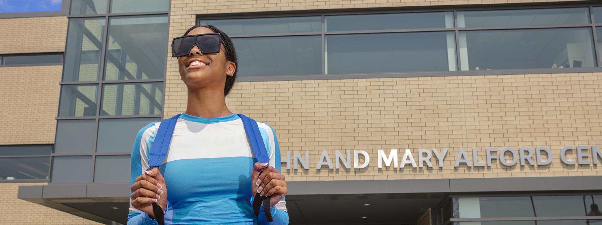 A female student walks out of the Alford Center with her head facing upward while smiling.
