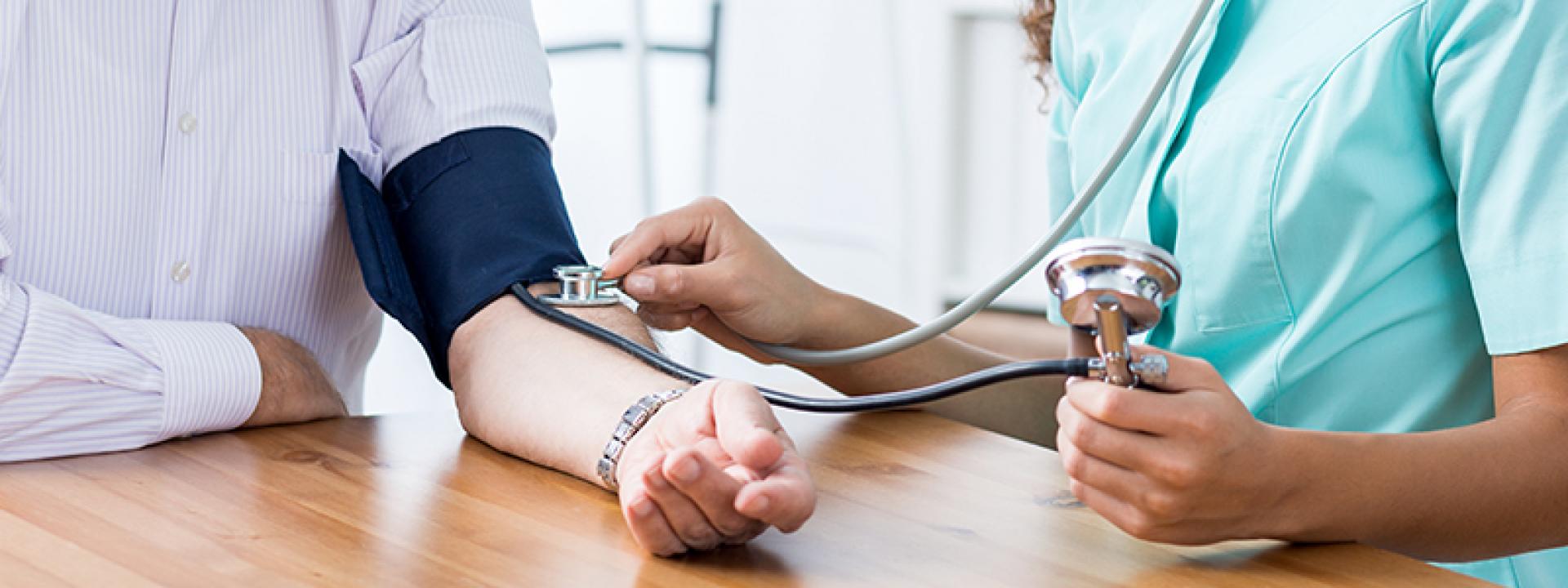 Female nurse taking blood pressure of elderly male, both sitting at table