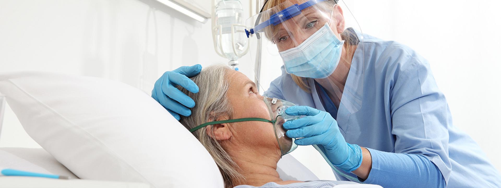 a respiratory therapist places an oxygen mask on an elderly patient in a hospital bed. 