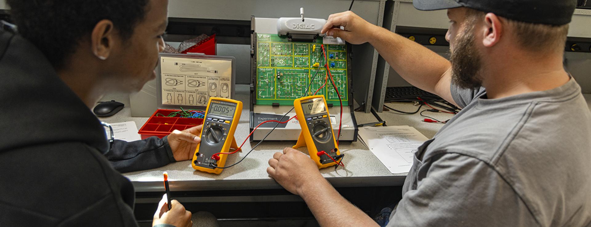 Two students sit at an electrical circuit board in an engineering lab at COTC.
