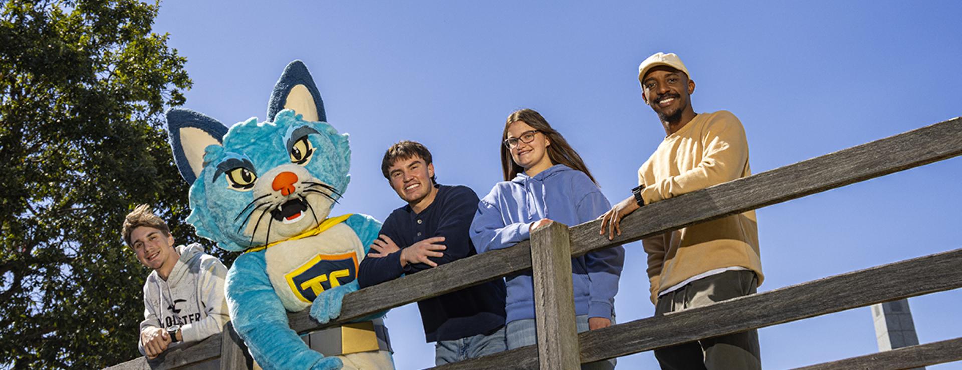 Four students stand on the iconic bridge on COTC's Newark campus with TC the mascot.