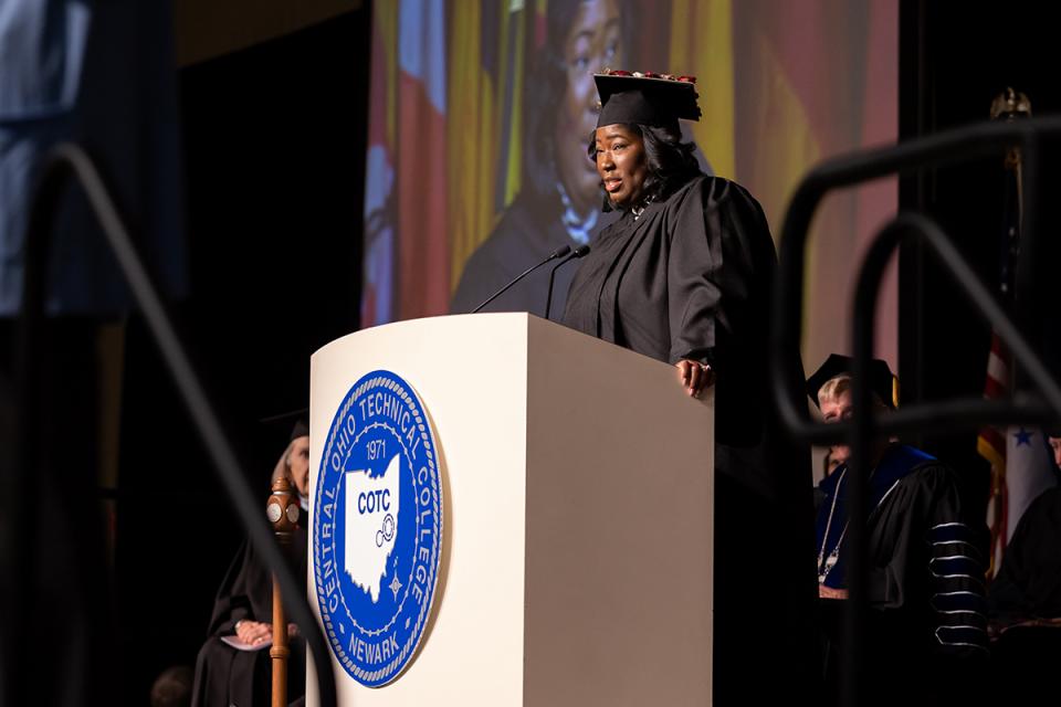 Affiong Hawkins dressed in academic regalia speaks to graduates from a podium at commencement.