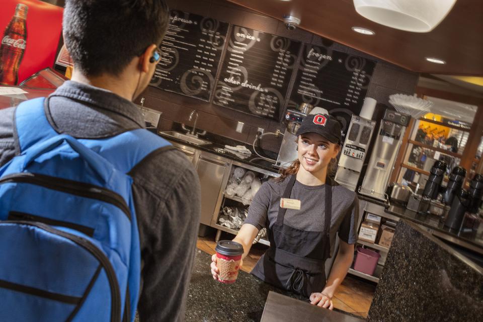 A student employee at the Bean counter hands a coffee cup to a student customer.