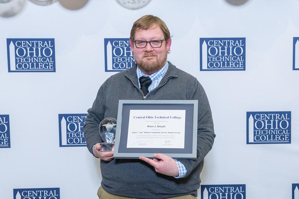 Brian Haught holds his Community Service Alumni Award and glass trophy.
