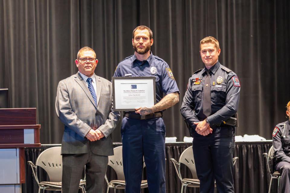 Commander James Rease, Joshua Oppenheimer and Deputy Chief Alan Horujko Joshua Oppenheimer stands on stage holding his award certificate with Commander James Reas and Deputy Chief Alan Horujko.