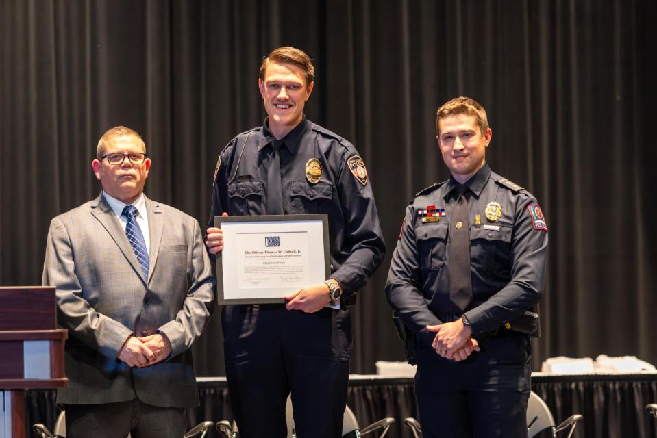Commander James Rease, Matthew J. Fries and Deputy Chief Alan Horujko. Matthew Fries stands on stage holding his award certificate with Commander James Rease and Deputy Chief Alan Horujko.