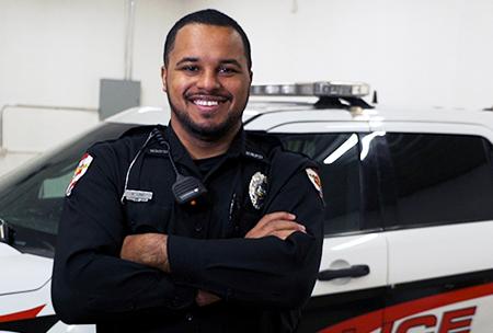 COTC graduate and peace officer DeLane stands next to a patrol vehicle. 
