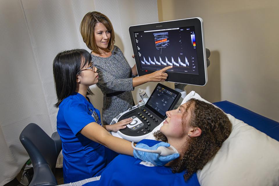 An instructor supervisors a student practicing an ultrasound scan on another student in scan lab.