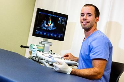 man in blue scrubs sitting at computer with diagnostic image loaded on screen