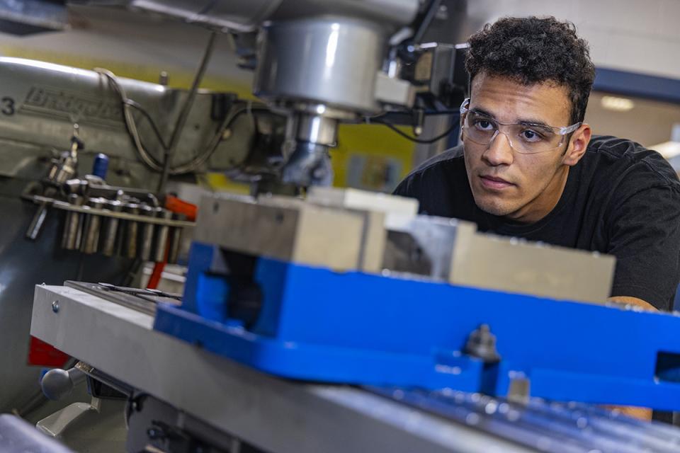 A student wearing safety glasses bends over to use a machine. 