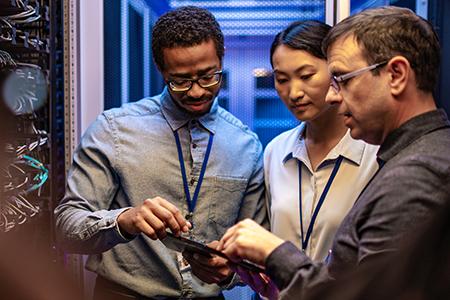 Two male and one female engineers using a digital tablet in a server room.