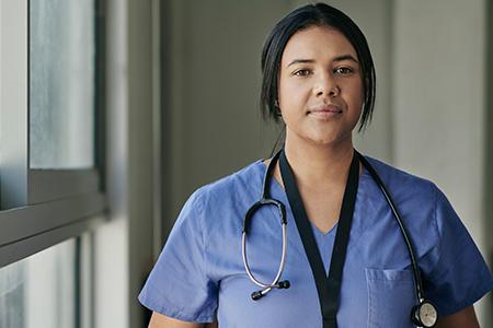 Portrait of a young female in nursing scrubs standing by a hospital window. 