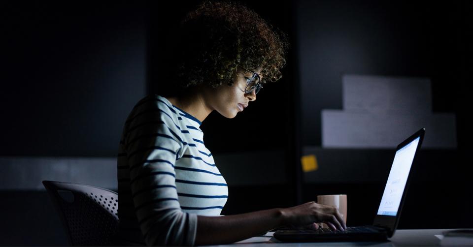 A female student studying late hours sitting with a laptop and typing.