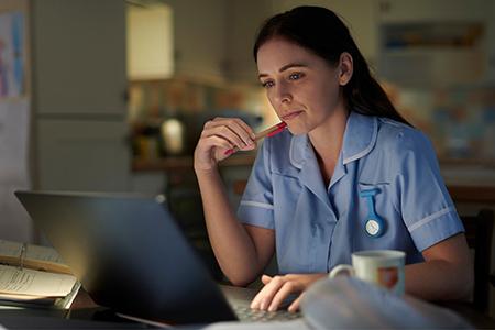 A female student studies from a laptop in her kitchen late at night. 