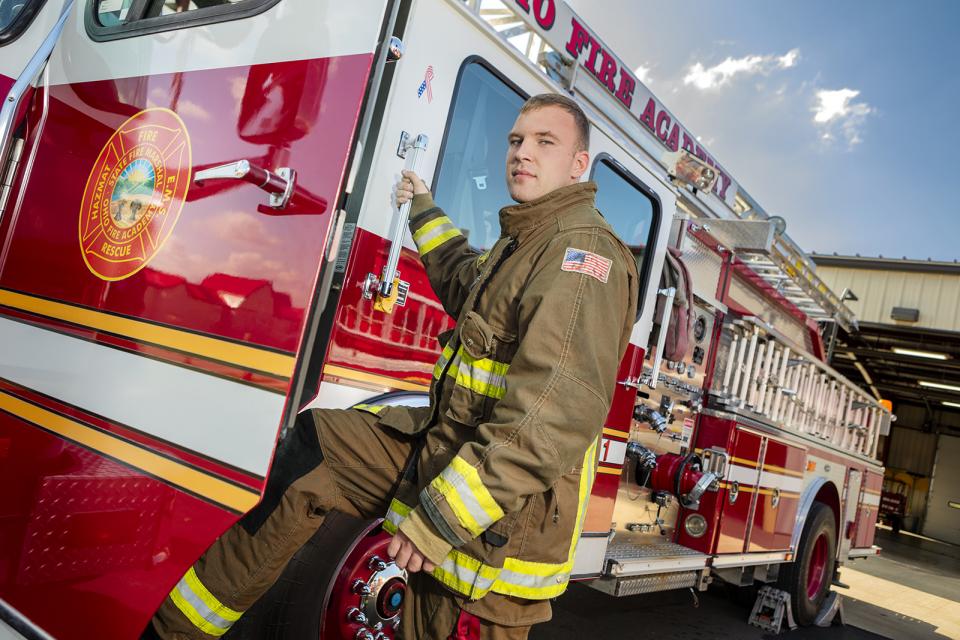 A student in firefighter uniform boards a fire truck. 