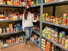 Woman standing near shelves of food with mask on smiling at camera