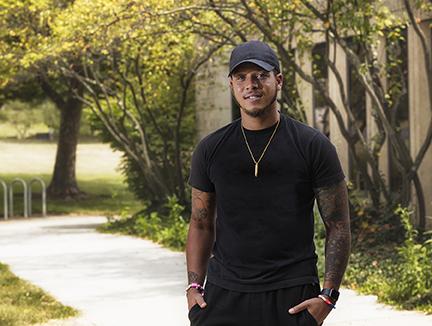 Male student wearing hat on sidewalk outside campus building
