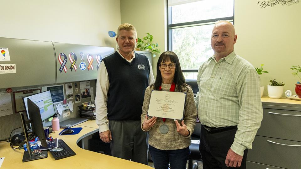 Charlene Ross holds her Excellence Award certificate standing with COTC President John Berry and COTC Provost Greg Ferenchak.