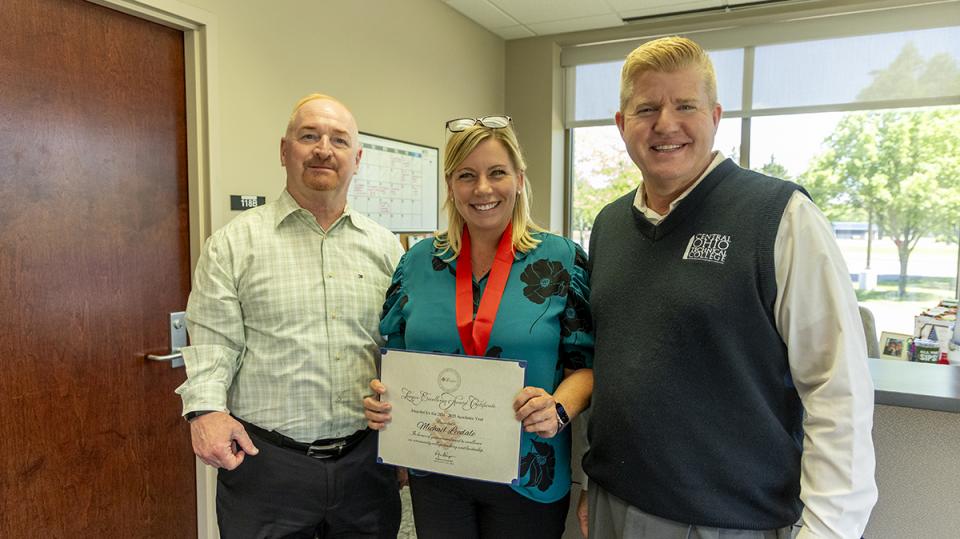 Michael Leedale holds her Excellence Award certificate standing with COTC President John Berry and COTC Provost Greg Ferenchak.