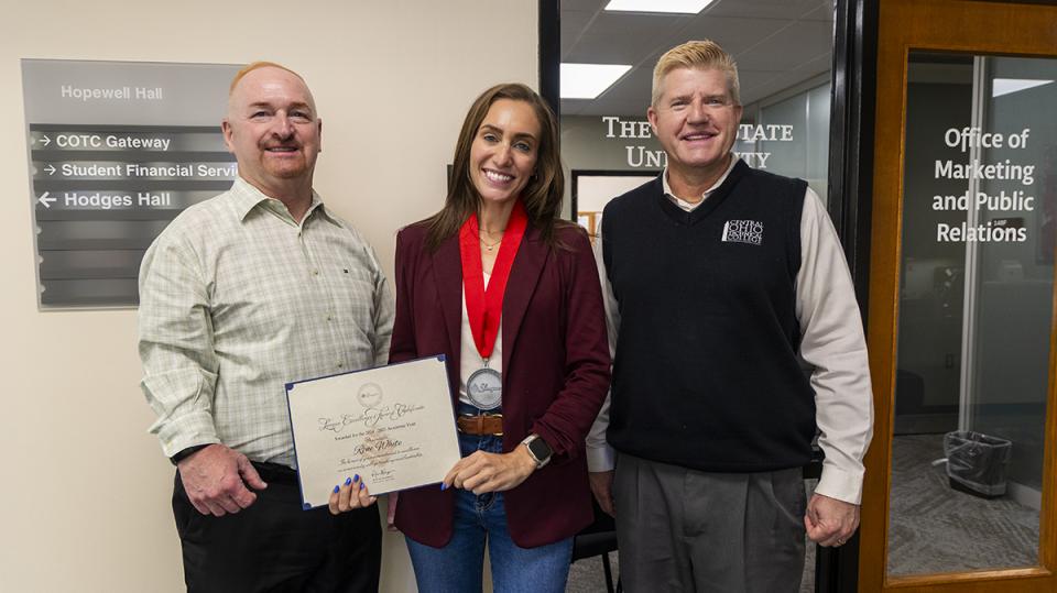 Rene White holds her Excellence Award certificate standing with COTC President John Berry and COTC Provost Greg Ferenchak.