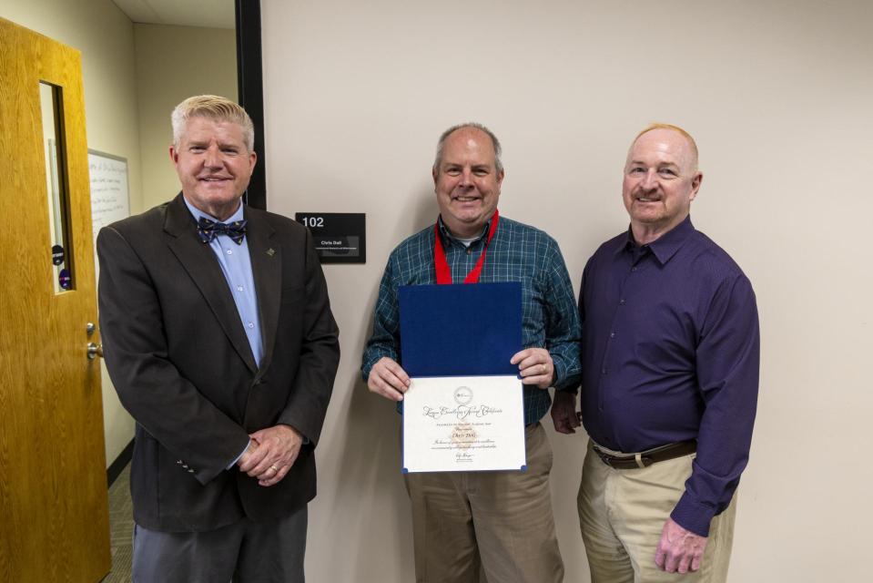 Chris Doll holds his League Excellence Award certificate while standing between COTC Provost Gregory Ferenchak and COTC President John Berry.