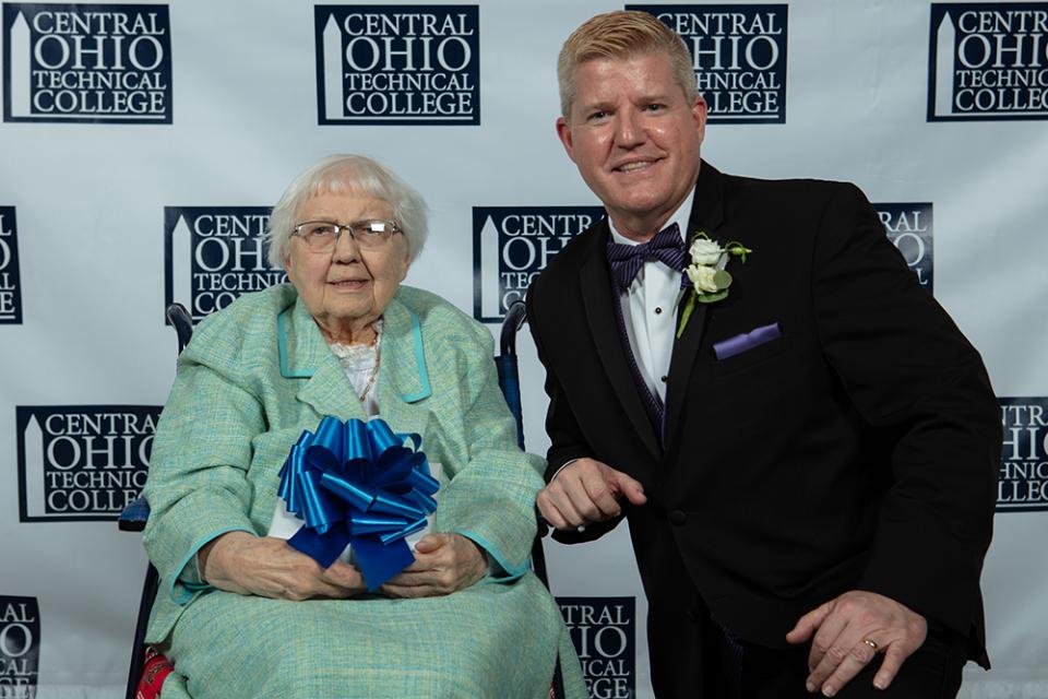 Clarissa Ann Howard sits with her Legends of Loyalty Award gift box next to a kneeling COTC President John Berry.