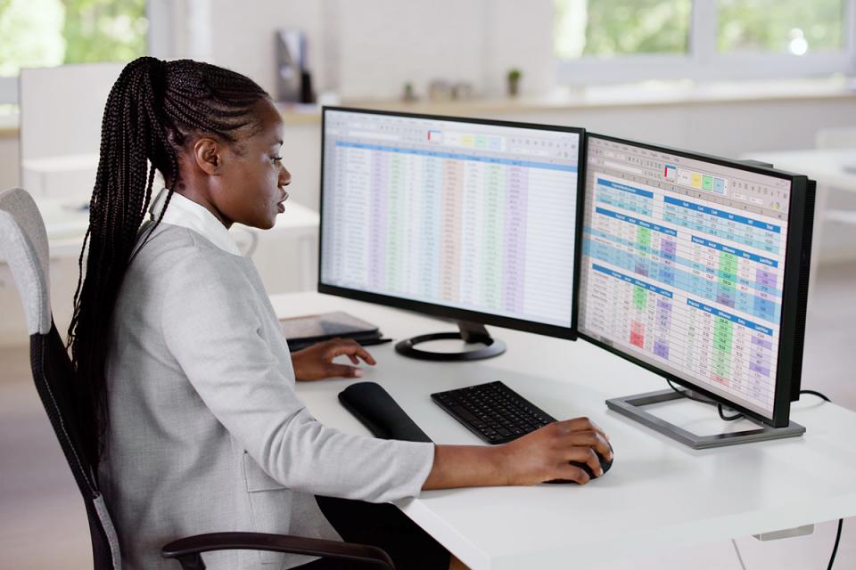 A woman sits in front of a computer with spreadsheets of data on the screen.