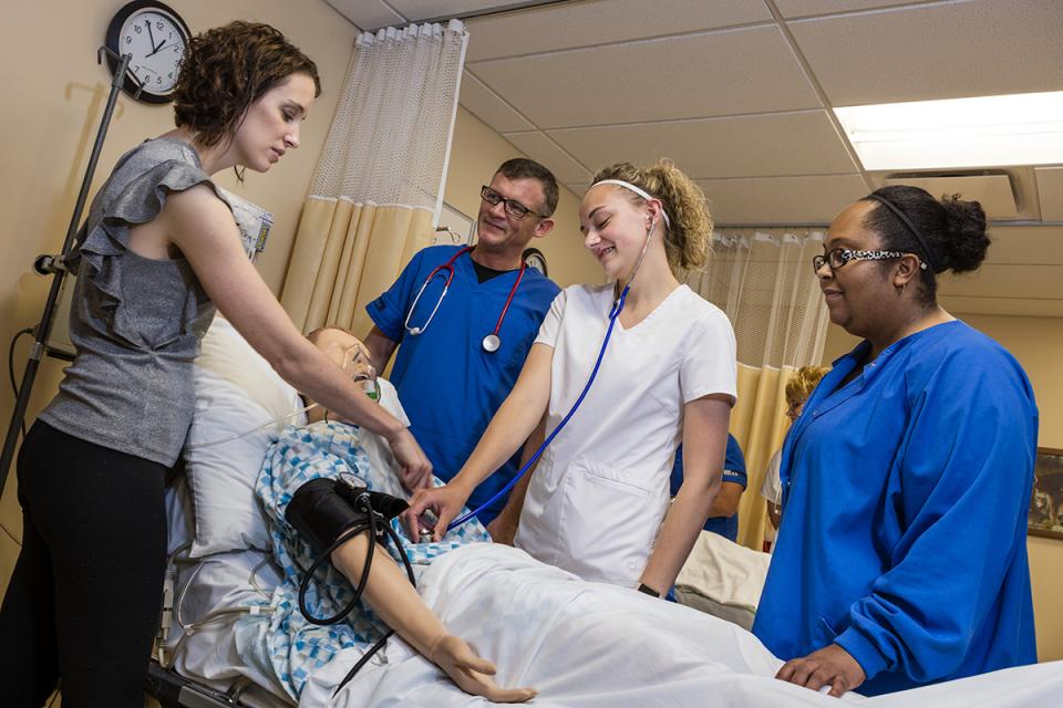 An instructor and three nursing students practice skills on a mannequin. 