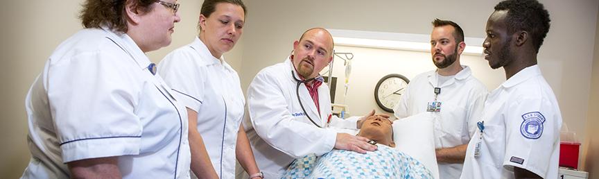 four students standing around professor showing technique on a dummy patient