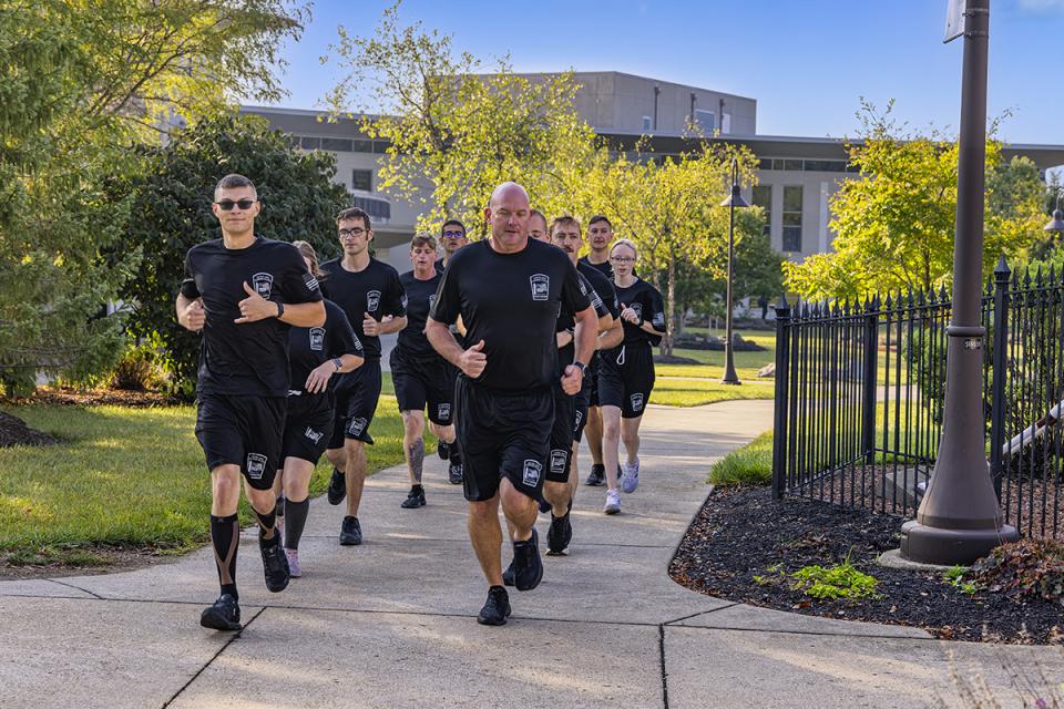 A group of police academy cadets runs with an instruction on the sidewalk of the Newark campus.