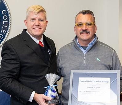 Man in suit and man with mustache wearing sweater holding framed certificate