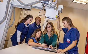A professor helps assists a student in obtaining an x-ray while classmates stand by watching.