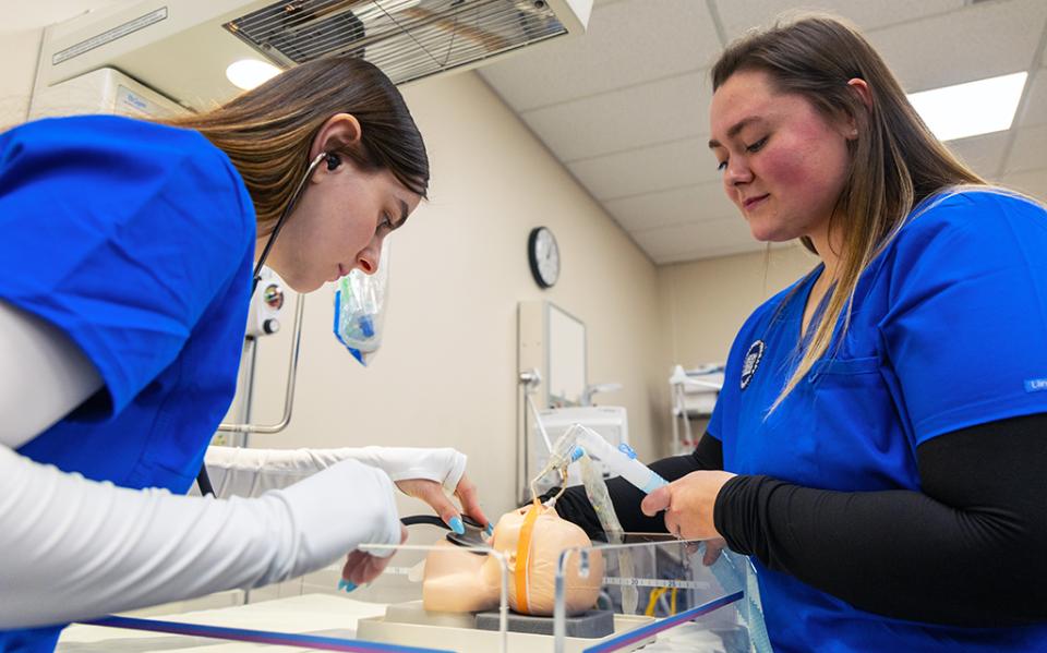 Two students fit a breathing apparatus on an infant-sized mannequin during a lab class at COTC.