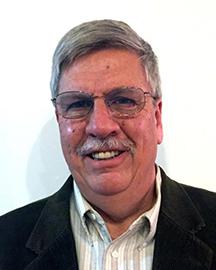 headshot of Gary Schworm wearing glasses, a moustache and a blazer and striped shirt