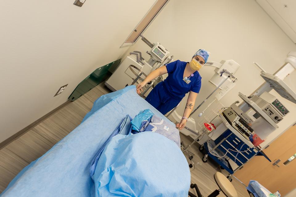 S student in scrubs and surgical mask prepares a medical bed for surgery.