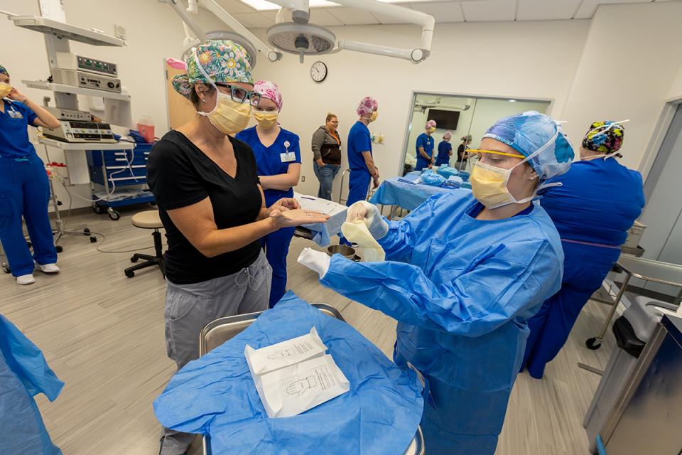 An instructor provides guidance to a student getting clothed for surgery. 
