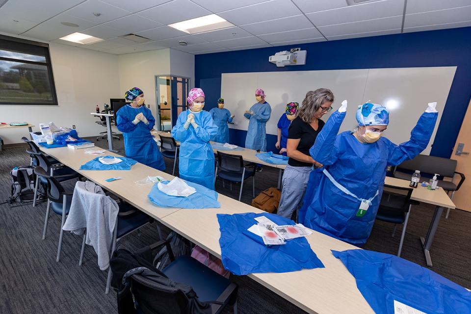 A student puts on a surgical gown with the help of an instructor. 