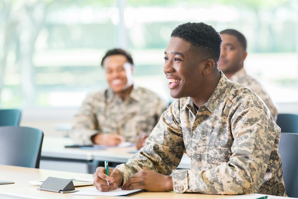 A student in Army fatigues smiles inside a classroom. 