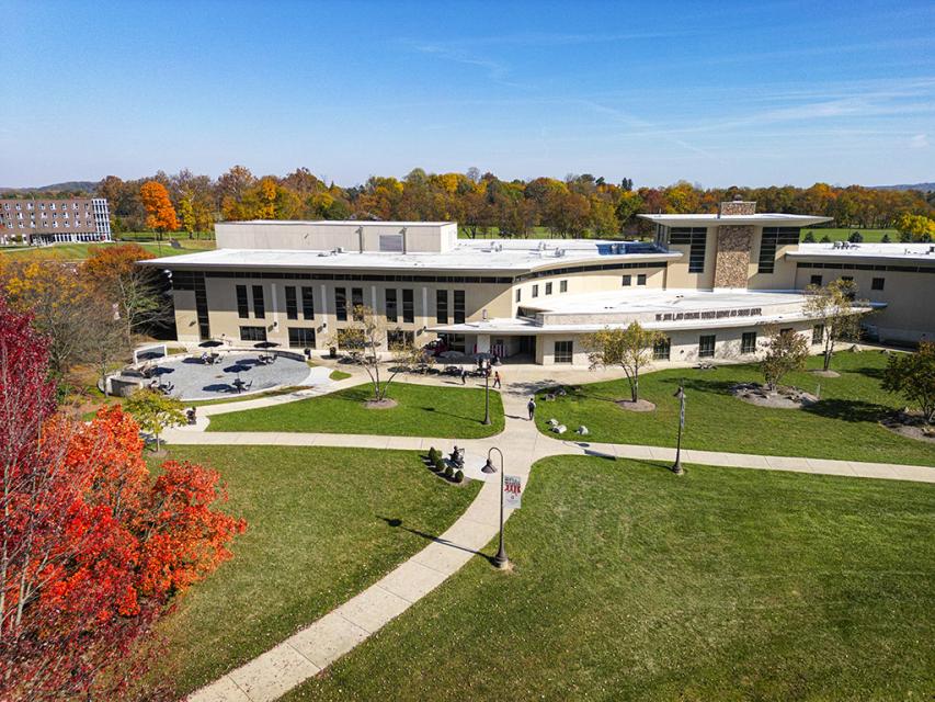 The exterior of the Warner Center from the backside where sidewalks lead to the door and trees are colored for autumn.