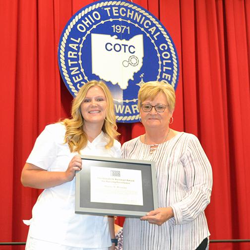 Woosley holding framed degree with faculty member (Ingersol) with COTC seal in background 
