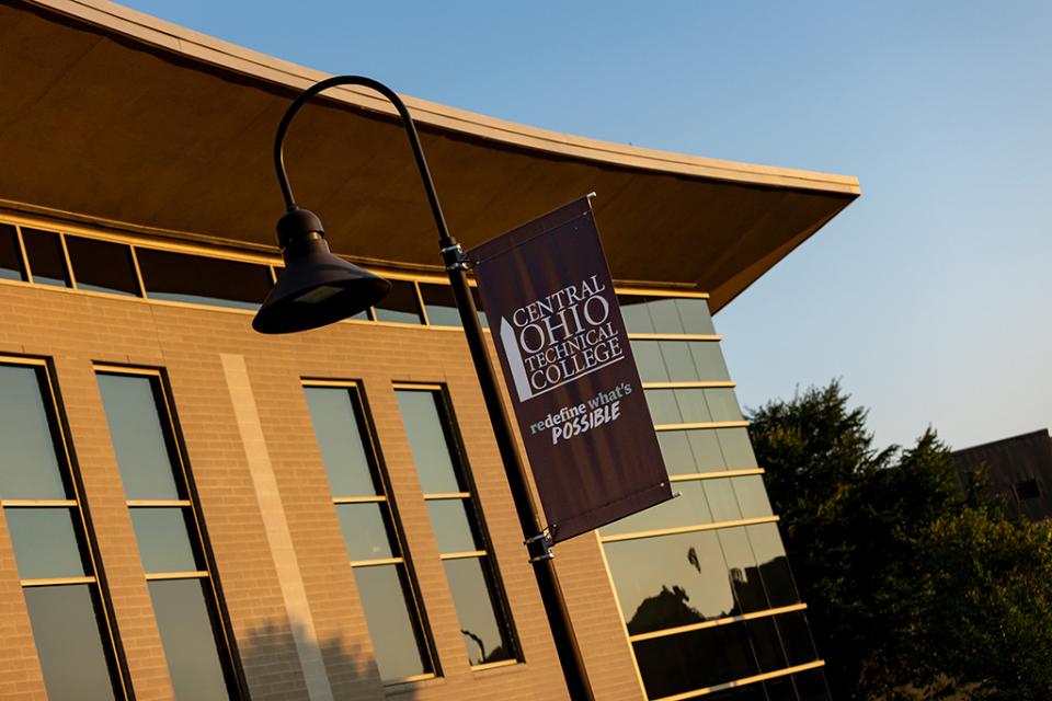 Sun shines on the facade of the Warner Center and an outdoor light with a COTC banner on it.
