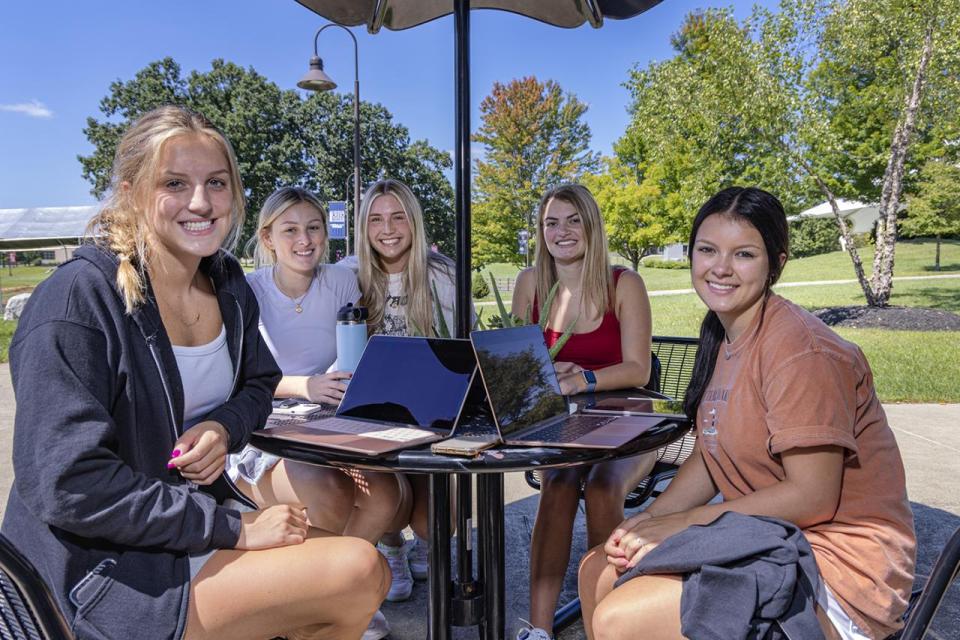 Five female students sit at a table outside on campus.