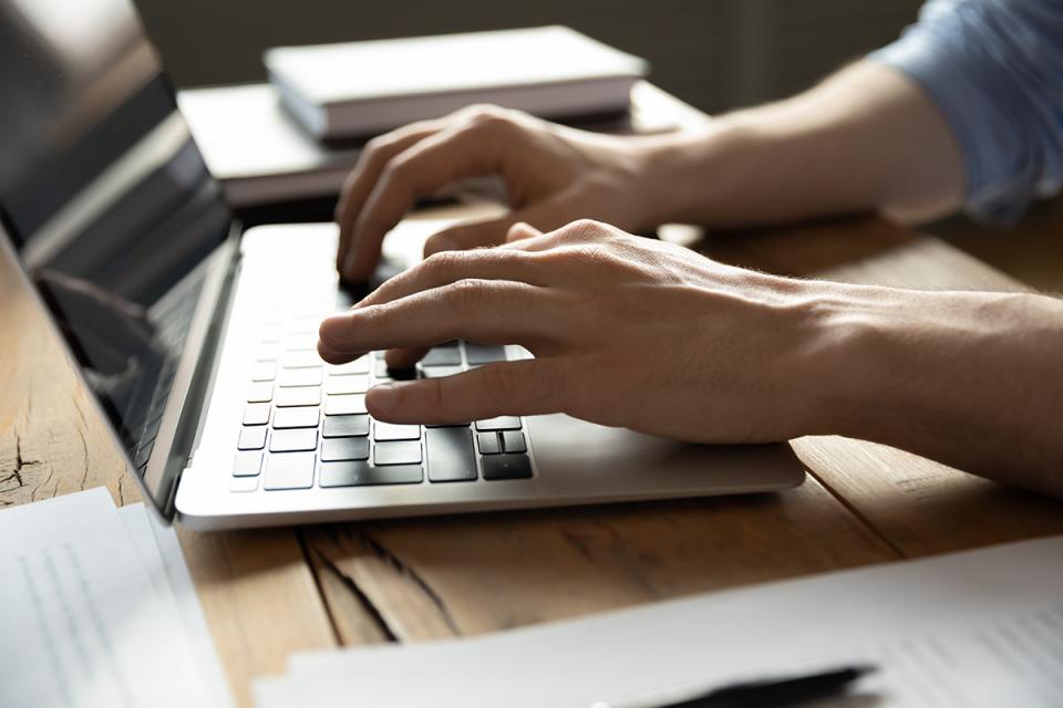 Close-up of a person's hands typing on the keyboard of a laptop. 